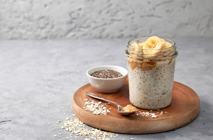 healthy diet breakfast overnight oatmeal with chia seeds, bananas, peanut butter, honey in a glass jar on a gray concrete background