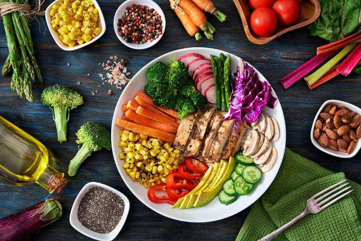 A plate of healthy, colourful food such as salad ingredients, nuts, chicken, vegetables.