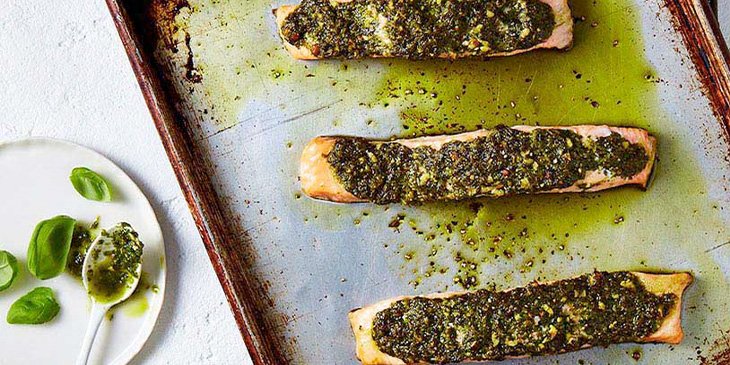 A rustic grey baking tray with baked salmon and pesto on top.