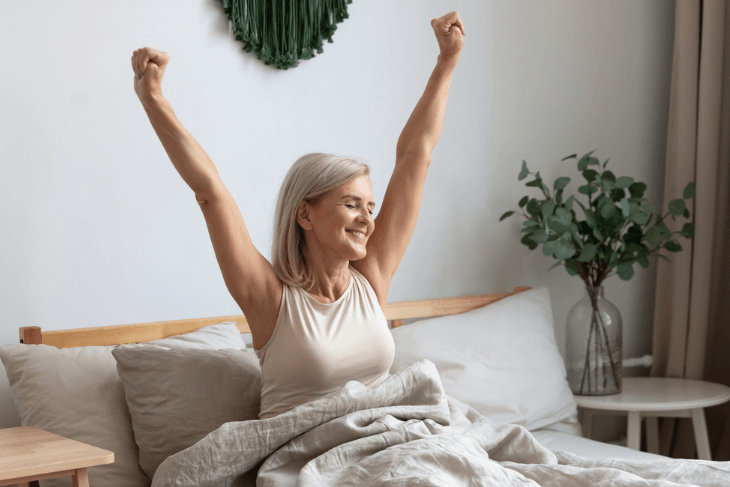 A woman over 40 stretching and smiling in bed.
